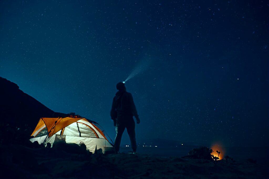 homme debout à côté d'une tente de camping portant une lampe frontale pendant la nuit