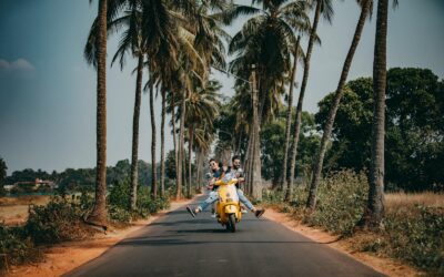 Un couple joyeux conduit un scooter jaune sur une route pittoresque bordée de palmiers, capturant l'essence du voyage et de l'aventure tropicale.