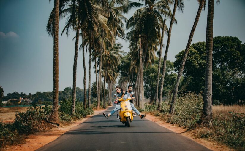 Un couple joyeux conduit un scooter jaune sur une route pittoresque bordée de palmiers, capturant l'essence du voyage et de l'aventure tropicale.